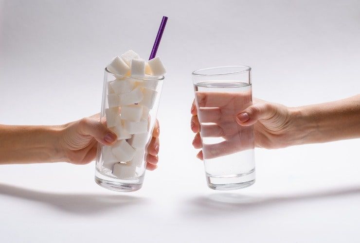 Bicchiere pieno di zucchero, davanti a un bicchiere di acqua pulita