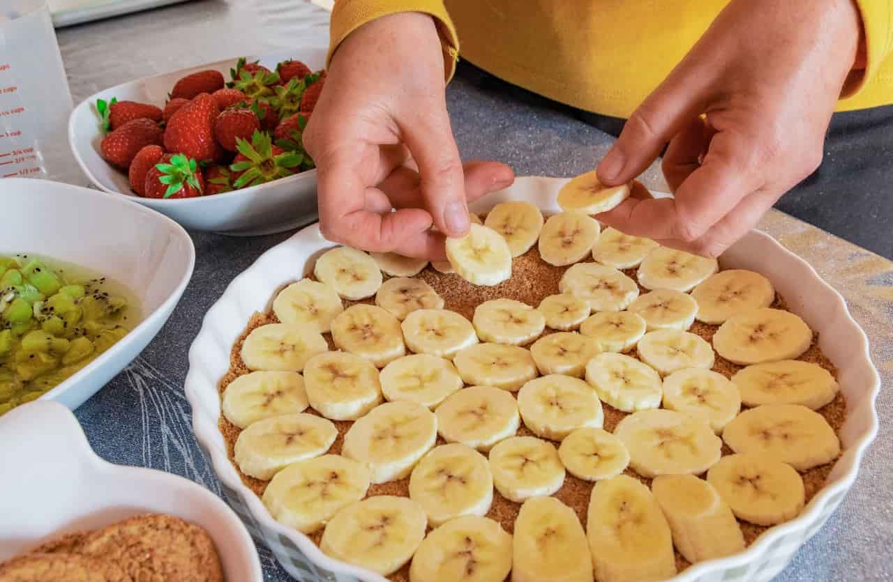 Mani femminili mettono fettine di banane in una teglia