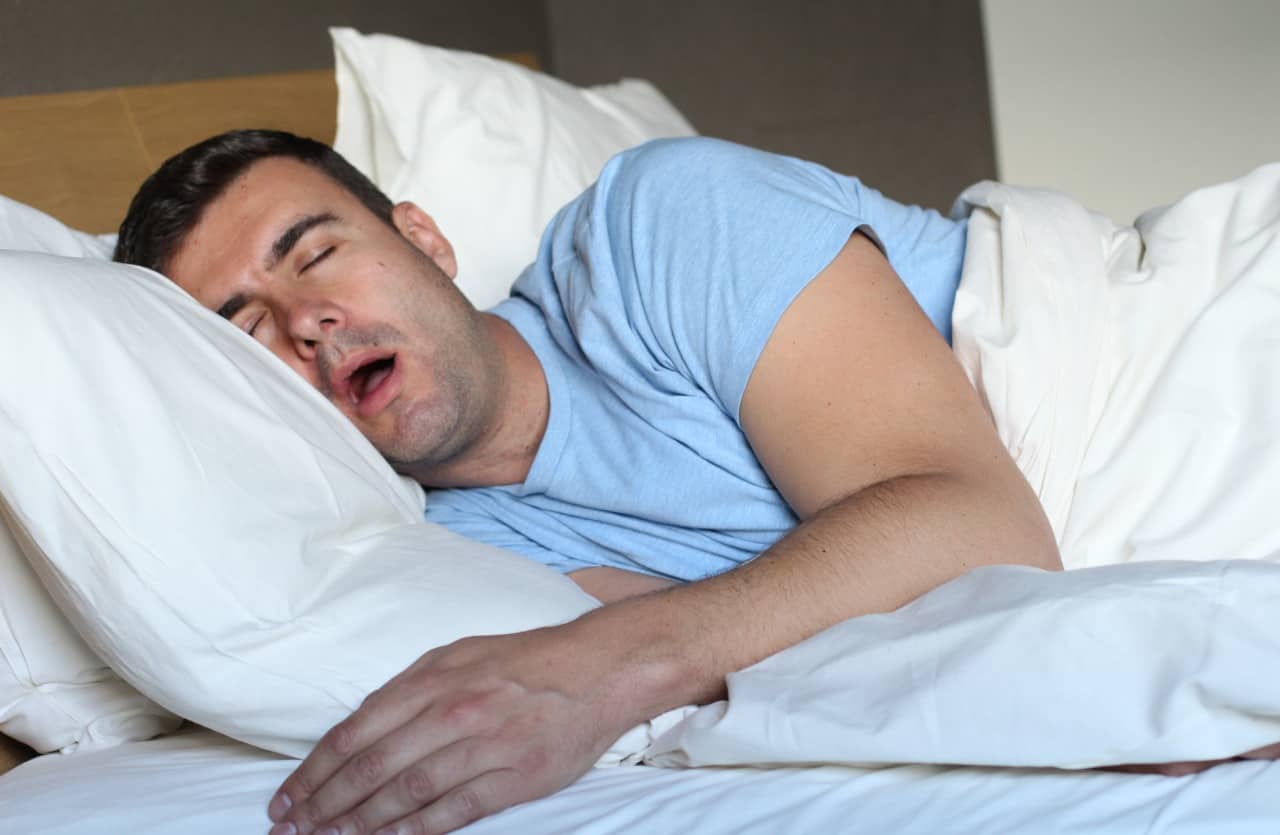 Mannen sover i sängen med öppen mun