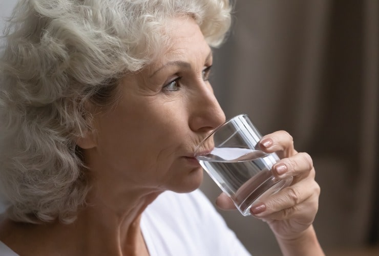 Donna matura beve un bicchiere d'acqua
