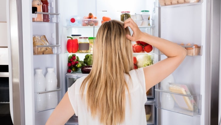 Donna guarda perplessa frigo aperto 